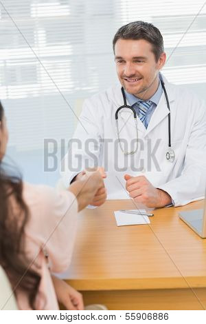 Smiling male doctor and patient shaking hands in the medical office