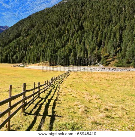 Scenic farm fields blocked bythe wooden fence. Shadow of the low fence beautifully lie on the grass. Alpine Valley in Austria. National Park Krimml