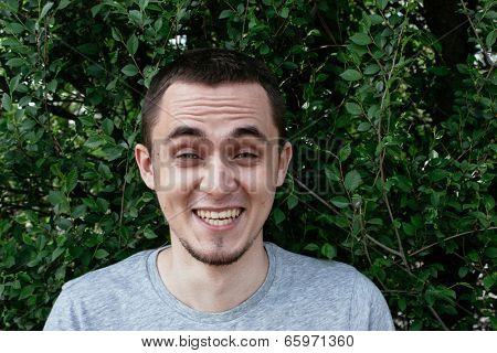 Young man with a goatee beard having a good laugh at a funny joke raising his eyebrows in mirth, standing against a leafy green tree