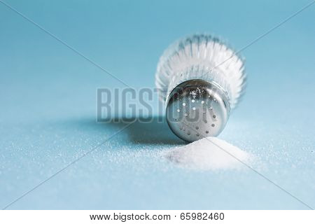 Spilled salt and saltshaker on blue background