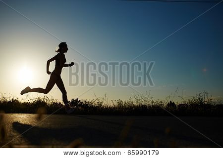 Silhouette of athletic girl running down the road to a sunset Silhouette of athletic girl running do