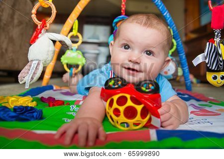 Happy and curious infant baby boy playing on activity mat
