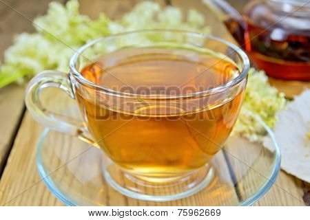 Tea from meadowsweet in glass cup and teapot on board