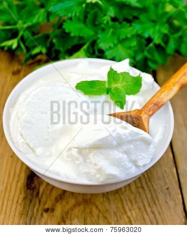 Yogurt in white bowl with mint and herbs on board