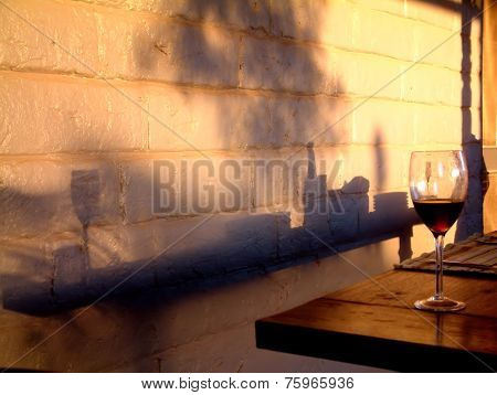 Wine glass on table with shadows on mud brick background