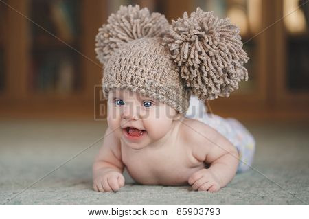 The newborn girl in a hat, lying on the floor, looking up.