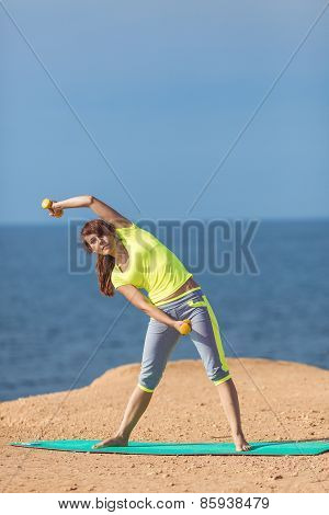A young woman fitness trainer, shows a set of exercises with dumbbells.