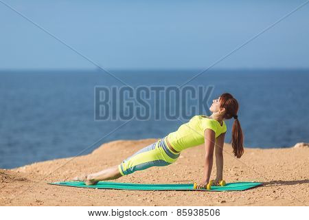 A young woman fitness trainer, shows a set of exercises with dumbbells.