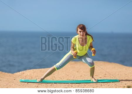 A young woman fitness trainer, shows a set of exercises with dumbbells.
