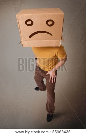Young man standing with a brown cardboard box on his head with sad face