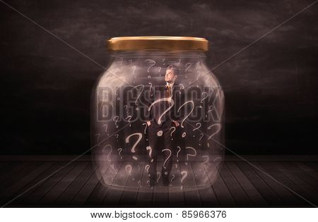 Businessman locked into a jar with question marks concept on background