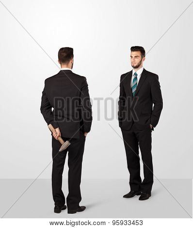 Two opposing businessman shake hands, one of them hiding a weapon behind his back