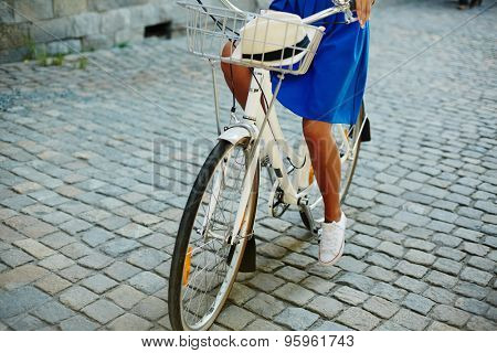 Young female in blue skirt riding bicycle in urban environment