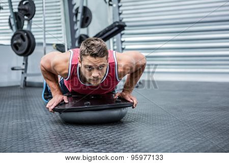 Portrait of muscular man using bosu ball in crossfit gym