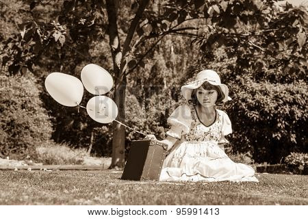 Sad and disappointed young girl sitting with her suitcase alone in the garden.