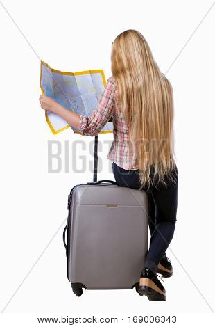 back view of woman traveler sitting on their suitcases and looking for a route map. backside view of person. Isolated over white background. Long-haired girl sitting on a suitcase and looking at map