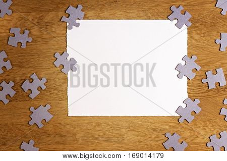White torn paper piece surrounded by puzzle pieces on wooden background. Top view. Copy space for text. Toned