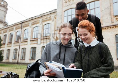 Multiethnic group of happy young people reading book outdoors at the unversity campus