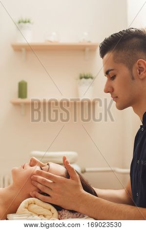 Young handsome man touching woman head free space. Male masseur massaging brunette at beauty salon, side view. Health care, full body massage, relax, headache, resort concept