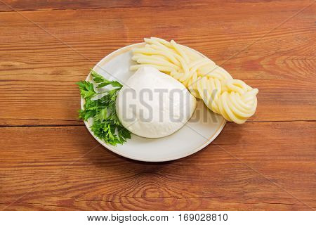 Ball of the fresh mozzarella cheese portion of the mozzarella cheese in the shape of strings twisted to form a plait and twig of parsley on the saucer on an old wooden surface