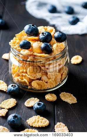 Healthy food concept. Close up of cornflackes with blackberries in jar on dark wooden background selective focus vertical.