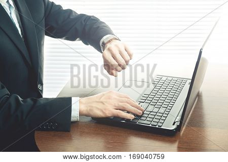 Business man working at office with laptop on his desk and looking at watch