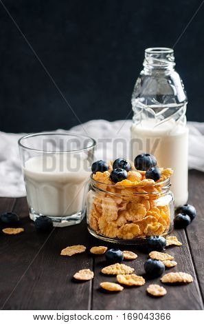 Cornflackes with blackberries and milk on dark wooden background selective focus vertical. Healthy food concept.