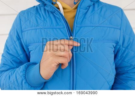 man buttons blue quilted jacket. cropped image of a man's hand fastens with a zipper on the jacket on a white background. close up