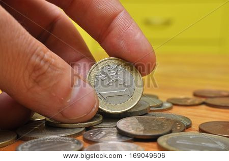 Man's hand hold one Euro coin under lot of different coins