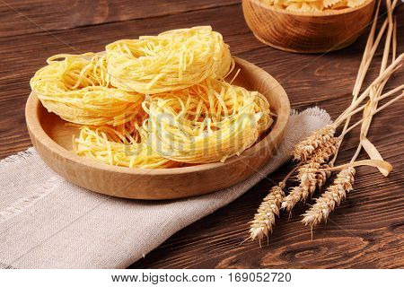 Raw pasta fettuccine and rye ears in a wooden bowl on the table