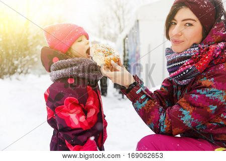 Mum feeds girl with bun on winter walk