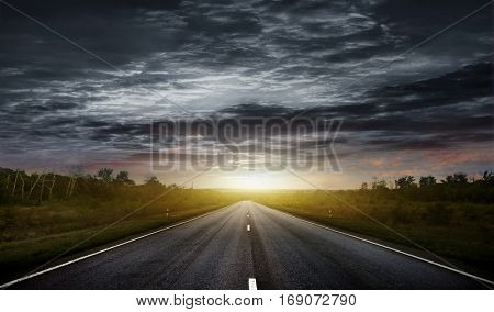 Long country road with white lines down the centre stretching off past a lone tree to the distant horizon 