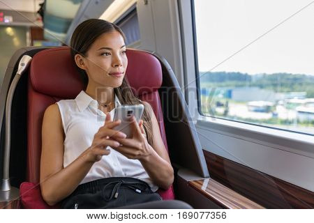 Asian woman relaxing in train seat while using smartphone app. Chinese businesswoman enjoying view texting on mobile phone. Travel lifestyle.