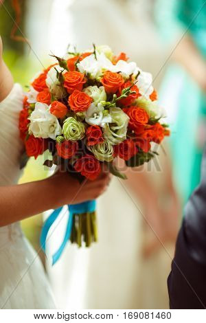 A wedding bouquet of orange and white roses is helb by a bride
