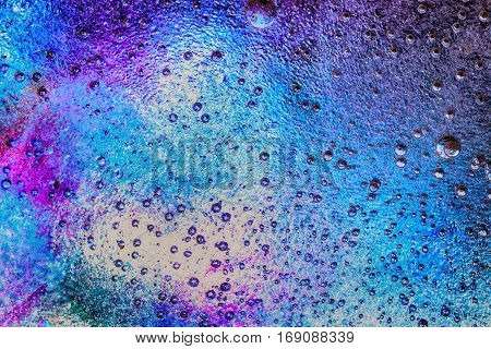 Frozen ice crystals with beautiful pink blue and purple colour below. Large and small trapped air bubbles all across the ice.