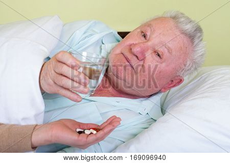 Picture of a bedridden elderly patient receiving his pills