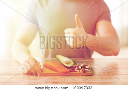 healthy eating, diet, gesture and people concept - close up of male hands showing thumbs up with food rich in protein on cutting board on table