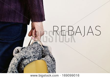 closeup of a young caucasian man seen from behind carrying a paper shopping bag full of clothes and the word  rebajas, sale written in spanish