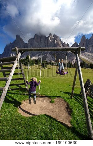 Girls sister swinging on a swing in the park Puez Odle. Italy