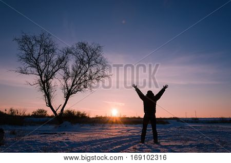 Tree In Snow Scene With Dramatic Sunset And Jumping Man Hands Up