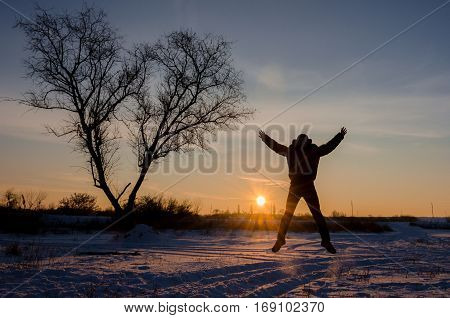 Tree In Snow Scene With Dramatic Sunset And Jumping Man Hands Up