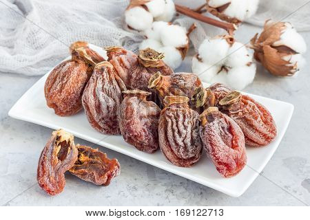 Several dried persimmon on white plate gray concrete background horizontal