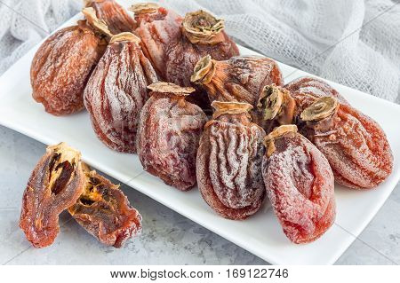 Several dried persimmon on white plate gray concrete background horizontal