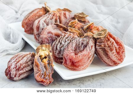Several dried persimmon on white plate gray concrete background horizontal