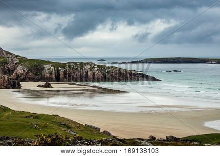 North Coast Scotland - June 6 2012: Durness Beach is a sandy patch looking north on a rough coast among rock cliffs and sprinkled pieces of rock. Under rainy sky with the light blue ocean gently flowing in.
