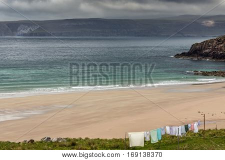 North Coast Scotland - June 6 2012: Line of multi-colored laundry hangs above Durness Beach a sandy patch looking north on a rough coast among rock cliffs and sprinkled pieces of rock.