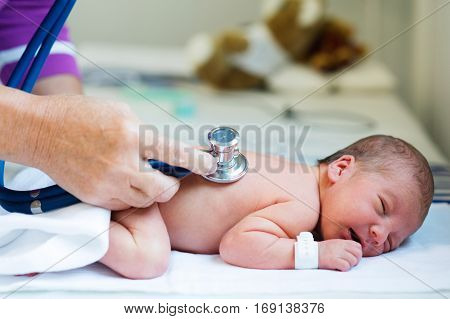 Unrecognizable doctor with stethoscope listening to hearbeat of cute newborn baby