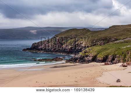 North Coast Scotland - June 6 2012: Cliffs descend on Durness Beach a sandy patch looking north on a rough coast among rock cliffs and sprinkled pieces of rock.