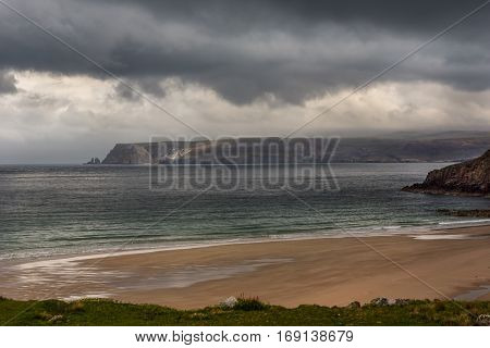 North Coast Scotland - June 6 2012: Huge cliffs tower over Durness Beach a sandy patch looking north on a rough coast among rock cliffs and sprinkled pieces of rock.