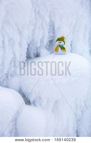Incredible beautiful interesting white snow froze in strange textures forms and snowflakes and among all this beauty there is a little snowman in a hat and scarf.